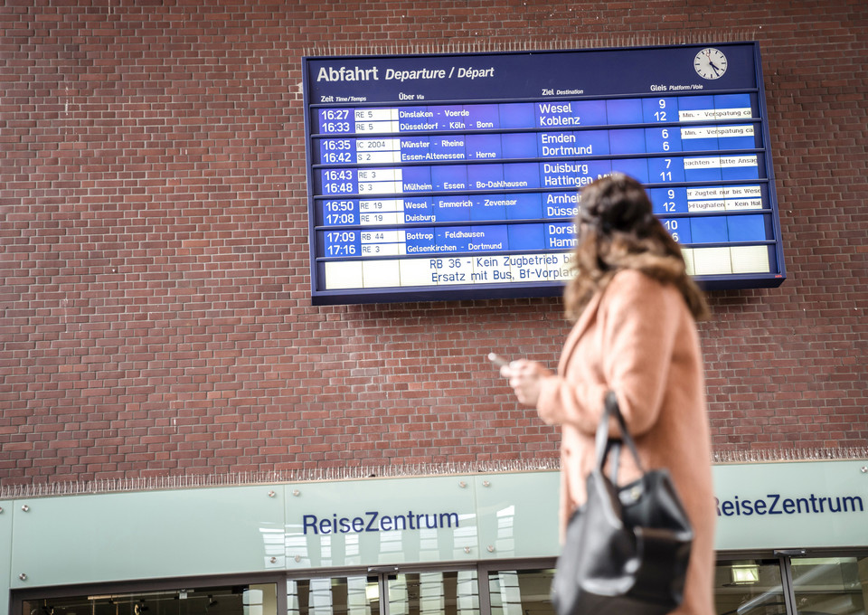 Eine Frau steht vor der Abfahrtsinfo-Tafel in der Bahnhofshalle
