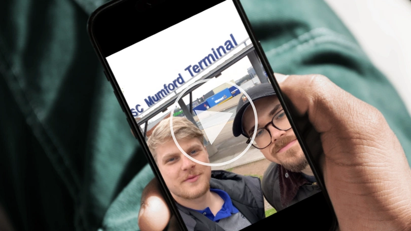 Ein Mensch hält ein Smartphone, man sieht einen Play Button und zwei Männer in die Kamera schauen.