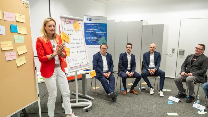 Eine Frau steht vor einem Flipchart und lehrt eine Gruppe von Menschen