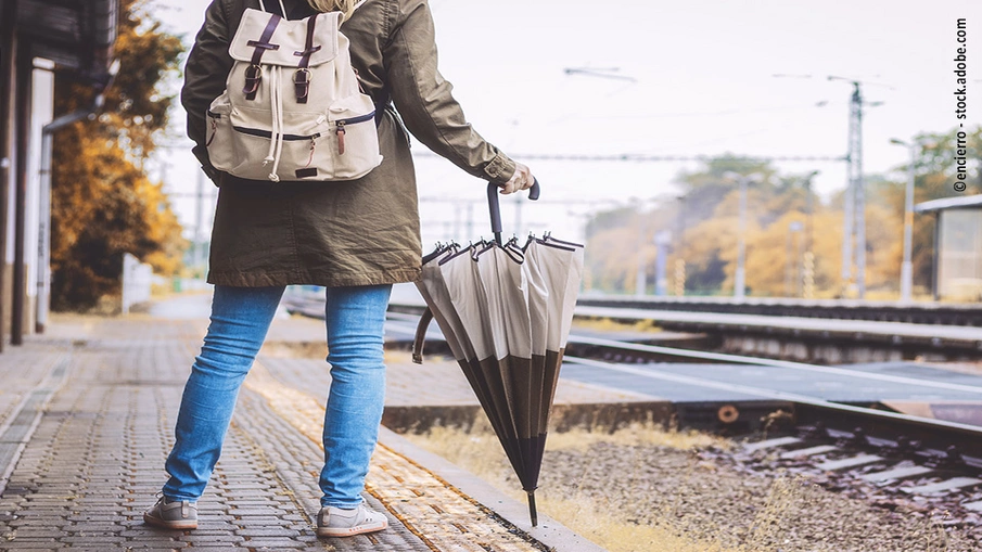 Frau mit Regenschirm wartet am Bahnsteig