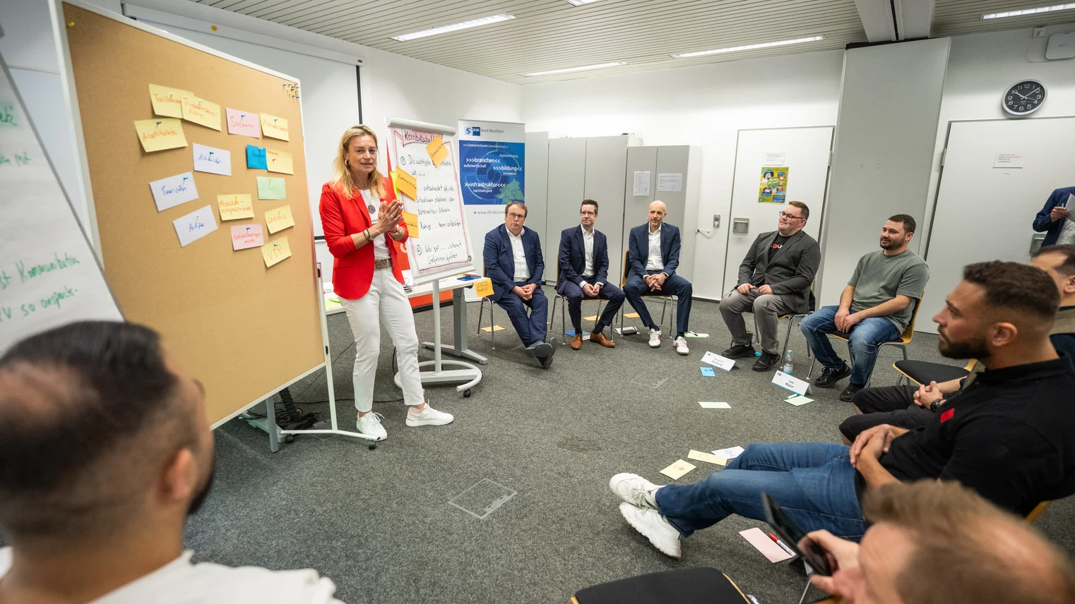 © Pöhnert / IHK Nord Westfalen Eine Gruppe von Personen sitzt im Kreis, eine Frau erklärt etwas und steht vor einem Flipchart