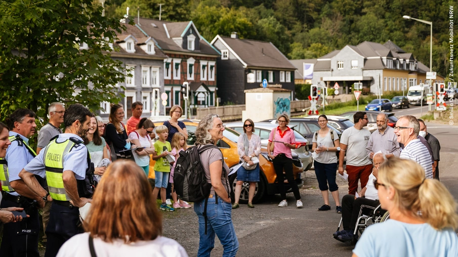Eine Gruppe von Personen beim Fußverkehrs-Check, u. a. mit Vertreter*innen der Polizei, Erwachsene, Kinder, ein Mensch im Rollstuhl