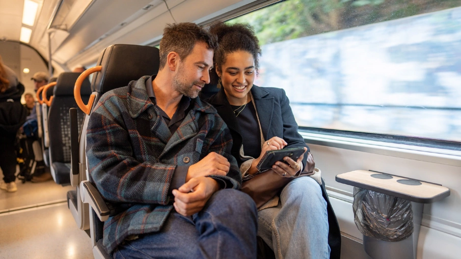 Ein Mann und eine Frau sitzen in einem RRX-Zug und schauen auf ein Tablet.