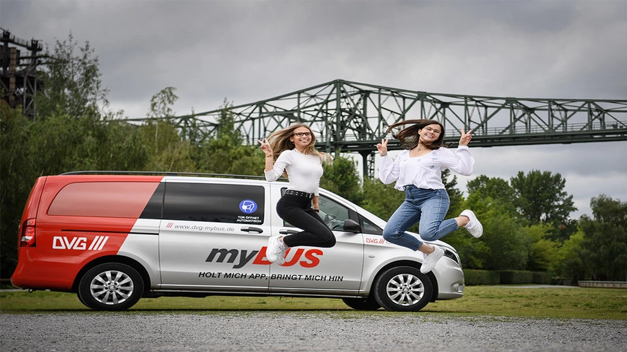 Zwei junge Frauen springen vor einem myBUS-Fahrzeug in die Luft.