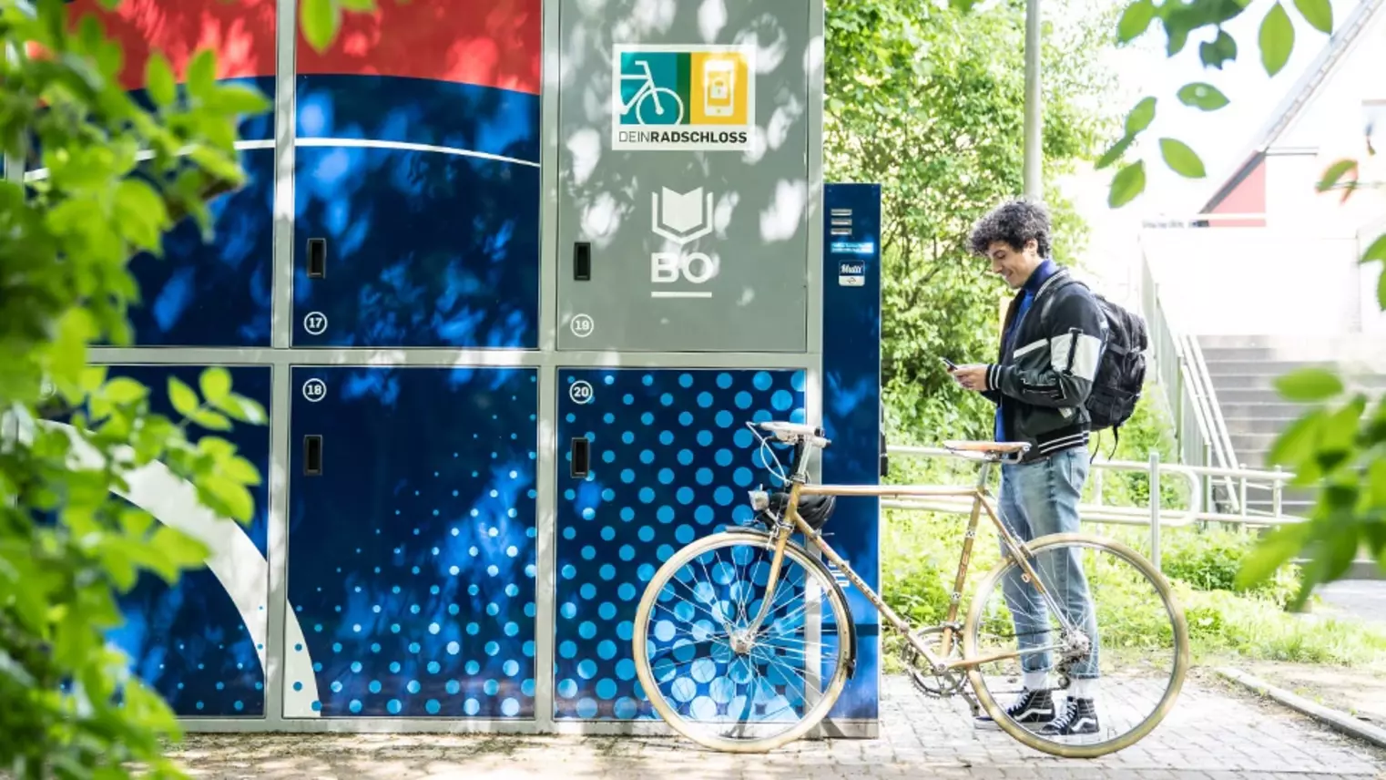 Ein Radfahrer steht mit seinem Smartphone in der Hand an einer Abstellbox von DeinRadschloss