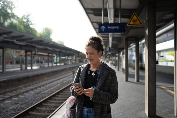 Frau mit Handy in der Hand steht am Bahngleis.