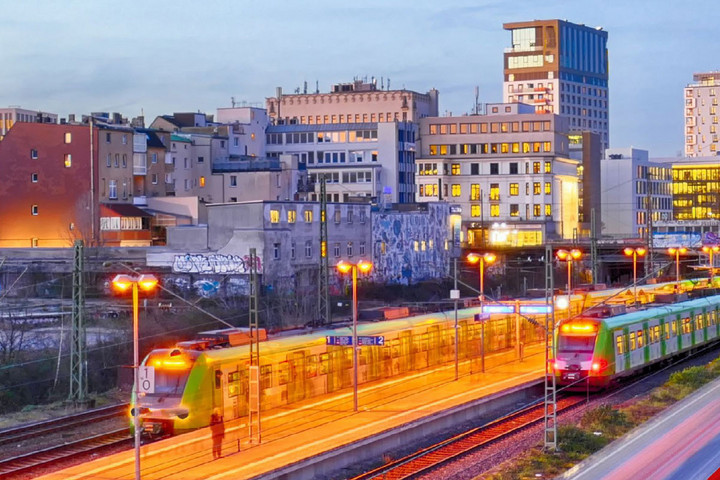 Blick auf einen Bahnhof am Abend. Züge stehen am Gleis, im Hintergrund sind Häuser zu sehen