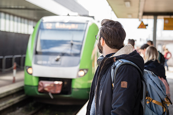 Ein Fahrgast, der auf die im Hintergrund einfahrende, grüne S-Bahn Rhein-Ruhr am Bahnhof wartet.