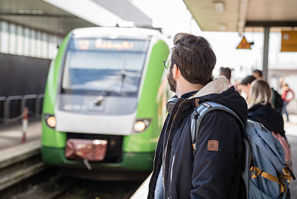 [Translate to English:] Ein Fahrgast, der auf die im Hintergrund einfahrende, grüne S-Bahn Rhein-Ruhr am Bahnhof wartet.