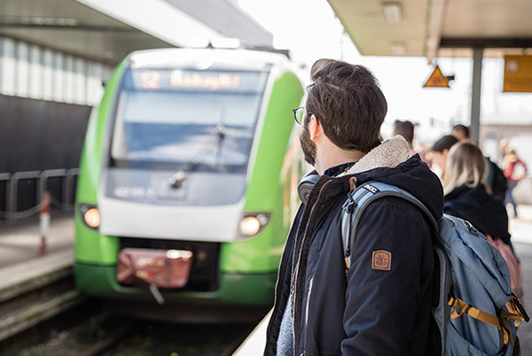 Ein Fahrgast, der auf die im Hintergrund einfahrende, grüne S-Bahn Rhein-Ruhr am Bahnhof wartet.