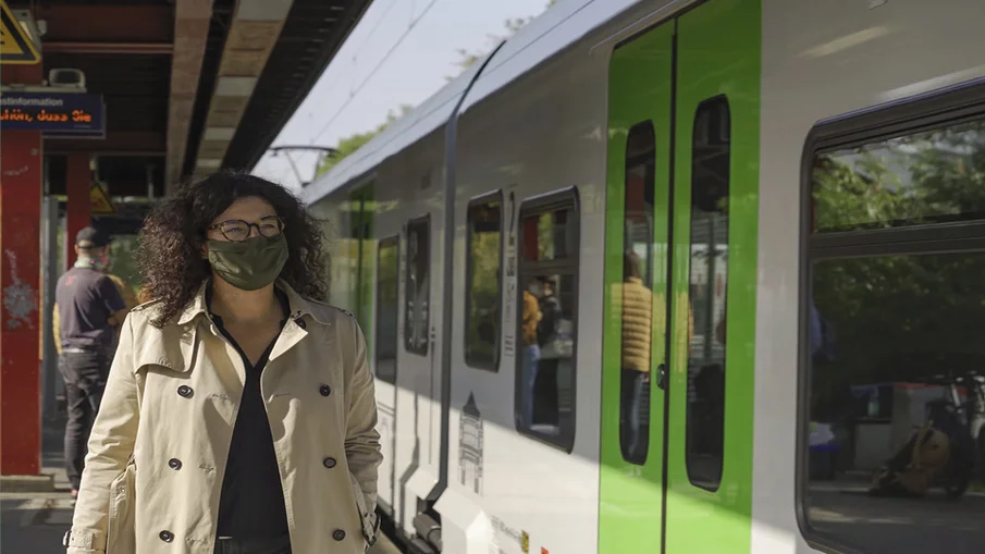 Eine Frau, die eine Maske trägt, läuft zu einem heranfahrenden Zug