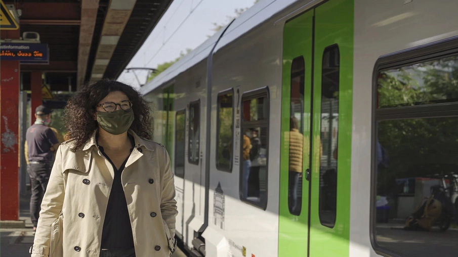 Eine Frau, die eine Maske trägt, läuft zu einem heranfahrenden Zug