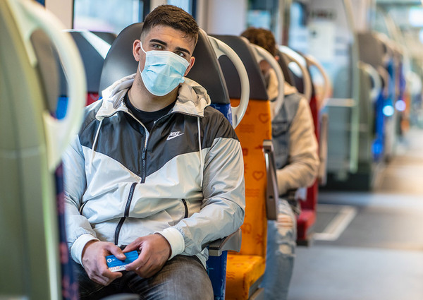 Mann sitzt mit Maske und Abo-Ticket in der Bahn