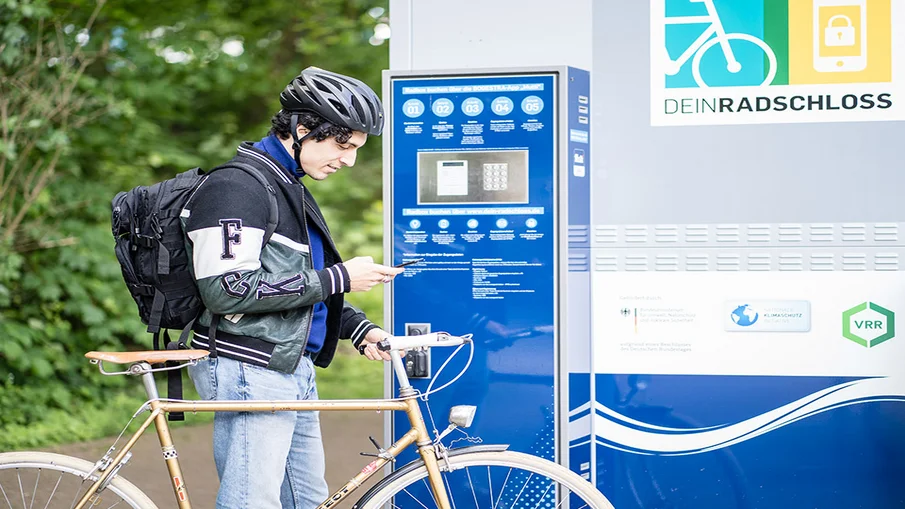A man stands with his bike in front of a DeinRadschloss station