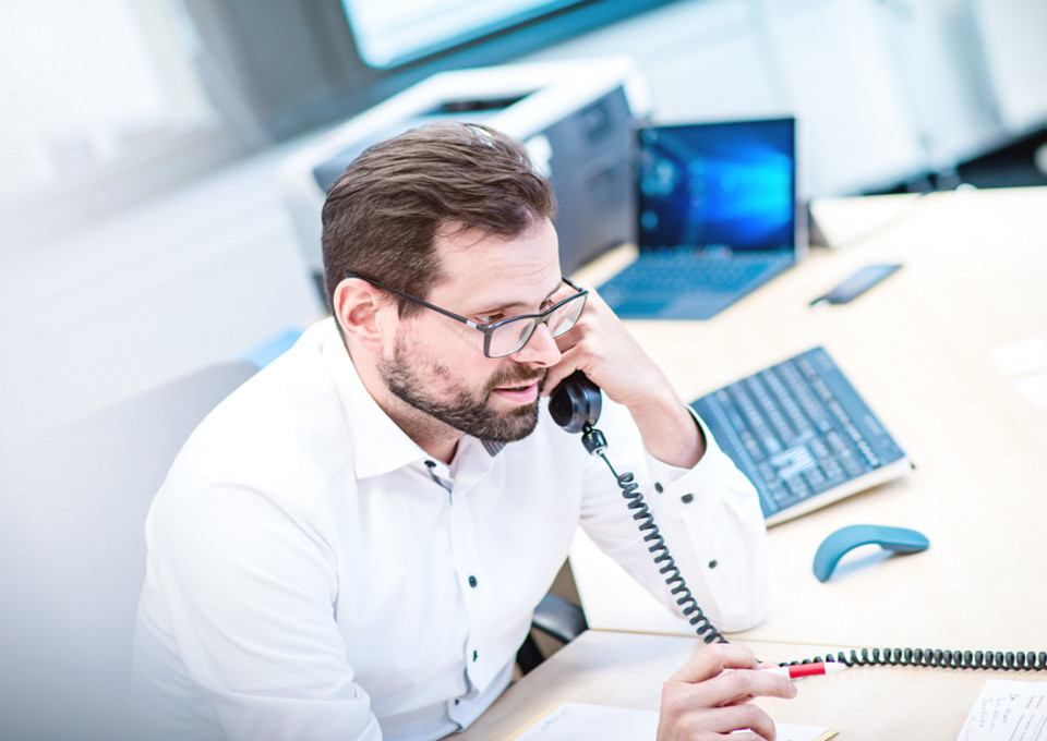 Ein VRR-Mitarbeiter am Telefon an seinem Schreibtisch sitzend.