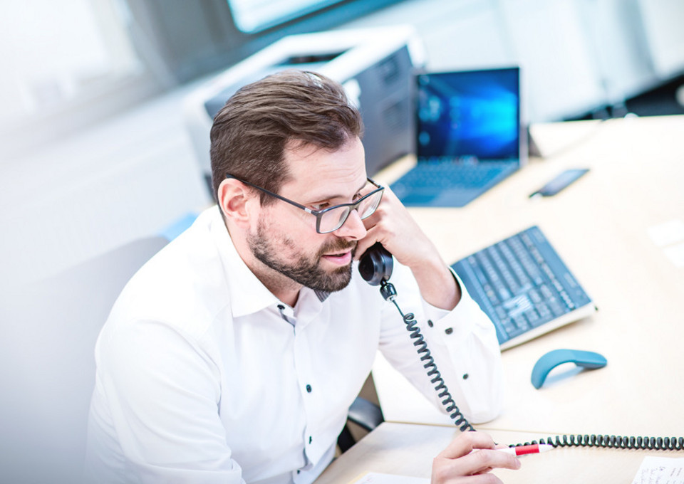 Ein VRR-Mitarbeiter am Telefon an seinem Schreibtisch sitzend.