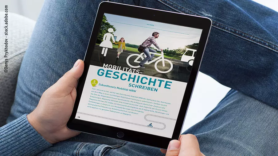 Person hält Tablet in der Hand, auf dem einen Seite aus der Jubiläumsbroschüre zu sehen ist