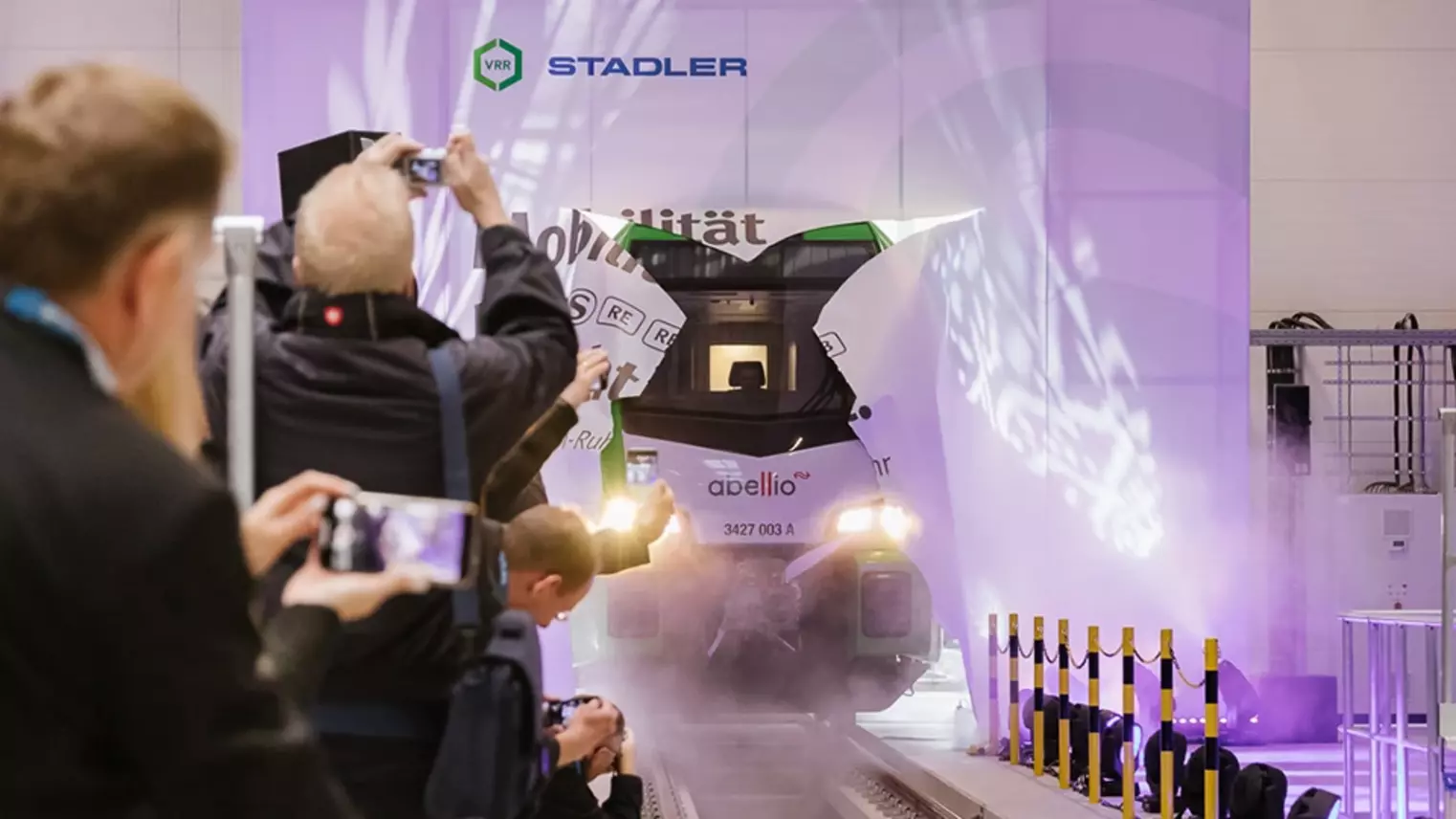 Eine neue S-Bahn im VRR-Design fährt zur Einweihungsfeier durch eine Papierwand in die Werkstatt ein