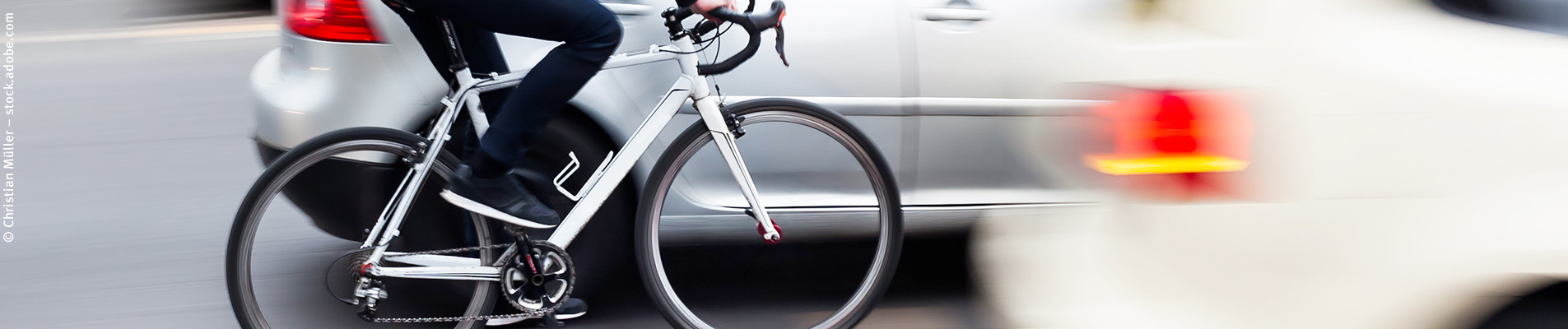 Das Bild zeigt einen Fahrradfahrer neben einem Auto fahrend.