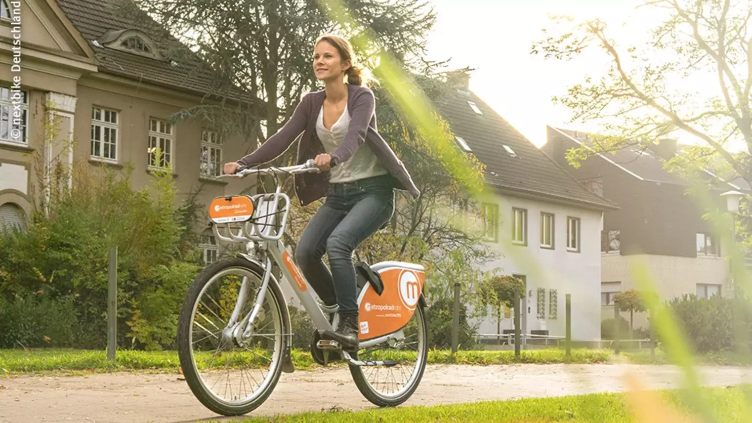 Eine Frau radelt mit einem Leihrad durch einen Park.