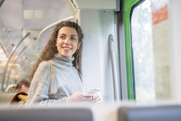 Eine Frau steht in der Bahn und hält ihr Handy in der Hand.