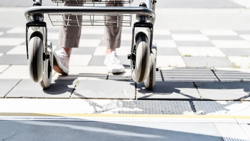 Blick aus einem Bus auf einen barrierefrei ausgebauten Bussteigt. Eine Person mit Rollator ist dabei, einzusteigen.