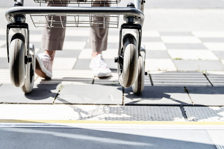 Blick aus einem Bus auf einen barrierefrei ausgebauten Bussteigt. Eine Person mit Rollator ist dabei, einzusteigen.