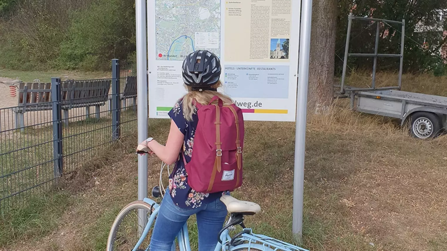 Eine Frau steht mit ihrem Fahrrad vor der Infotafel über den Ruhrtalradweg
