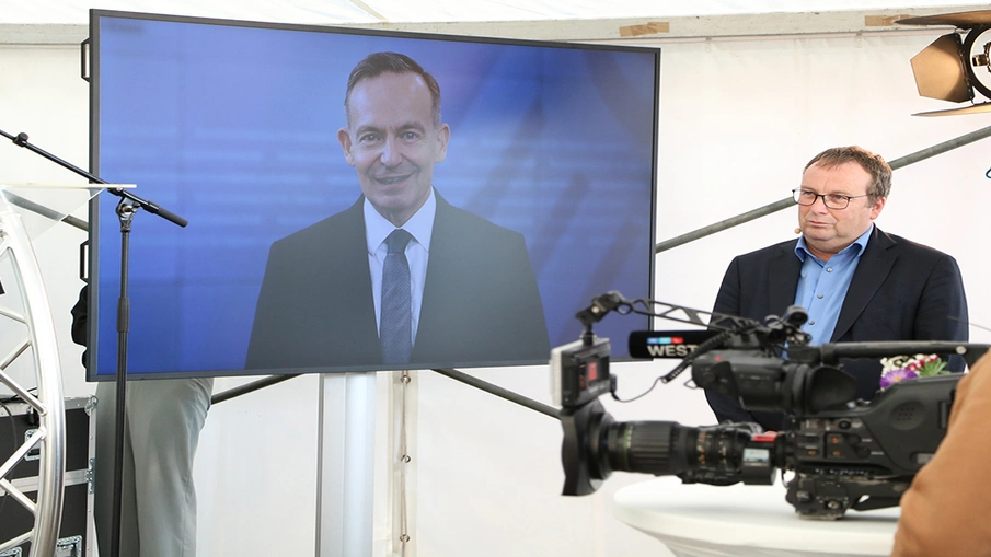 NRW-Verkehrsminister Oliver Krischer bei der zentralen Eröffnungsfeier zum Tag der Schiene 2024 in Mettmann, auf einem Bildschirm ist Bundesverkehrsminister Volker Wissing zu sehen
