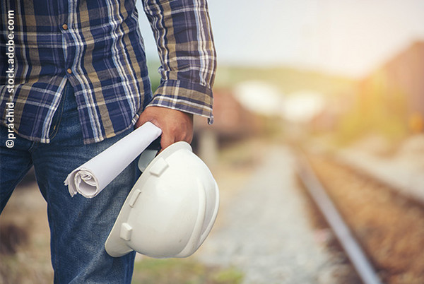 Ein Bauarbeiter mit Helm und Plan steht an den Gleisen