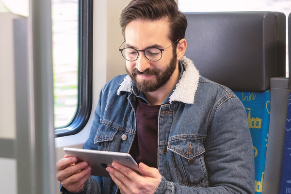 Ein Mann sitzt in der S-Bahn und schaut auf sein Tablet.