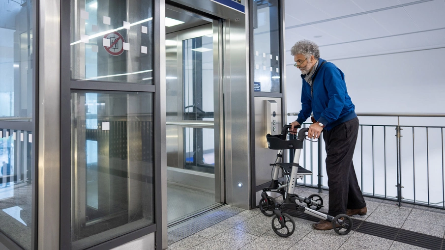 Ein älterer Mann mit Rollator steigt in einen Aufzug ein.