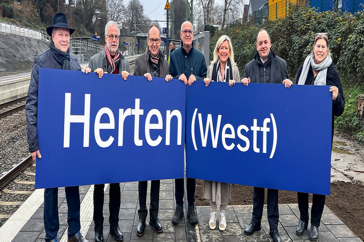 Teilnehmer*innen der feierlichen Eröffnung halten ein Schild mit der Aufschrift "Herten (Westf)" hoch