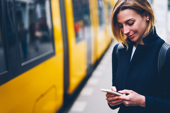 Eine Frau steht an einem Stadtbahn-Bahnsteig und schaut auf ihr Smartphone