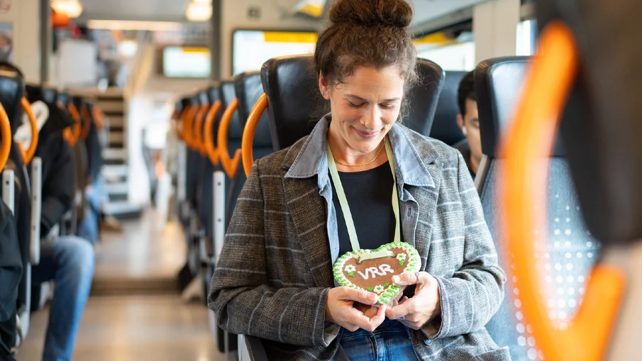 Eine Frau sitzt in einem RRX-Zug und blickt auf ein Lebkuchenherz mit dem Schriftzug "VRR"