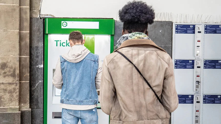 Zwei Personen stehen vor einem grün-weißen VRR-Ticketautomaten