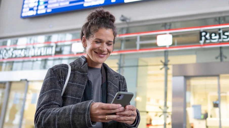 Eine Frau blickt in einem Bahnhof auf ihr Smartphone