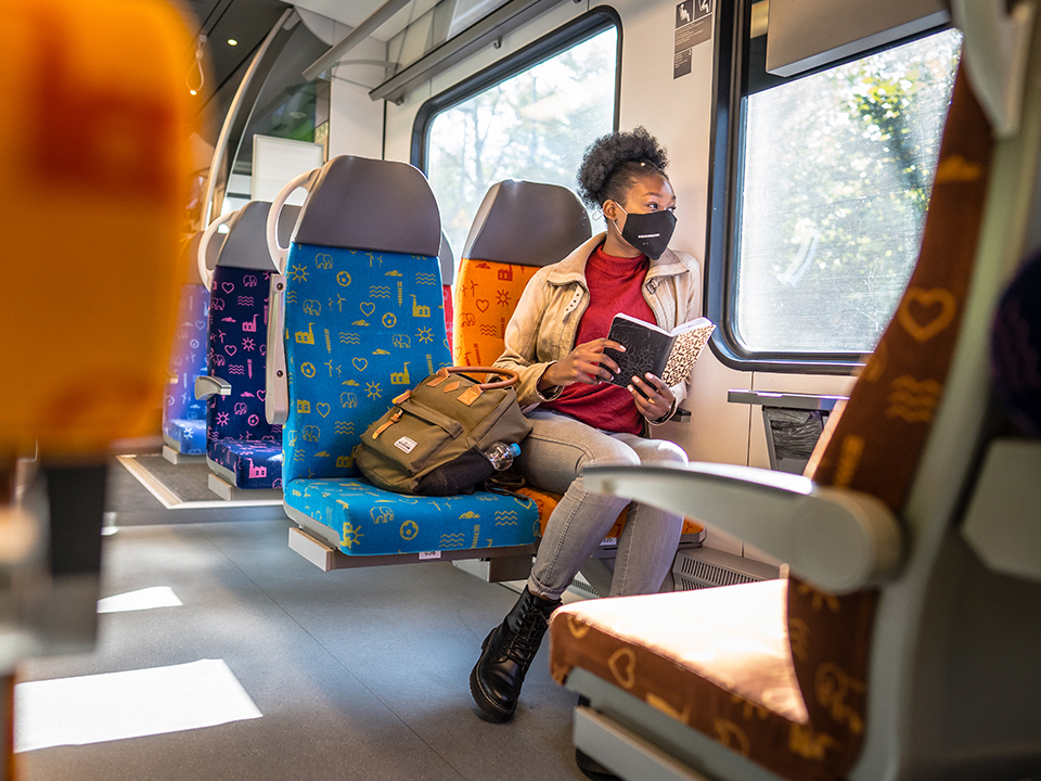 Eine Frau sitzt entspannt mit Maske und einem Buch in der S-Bahn