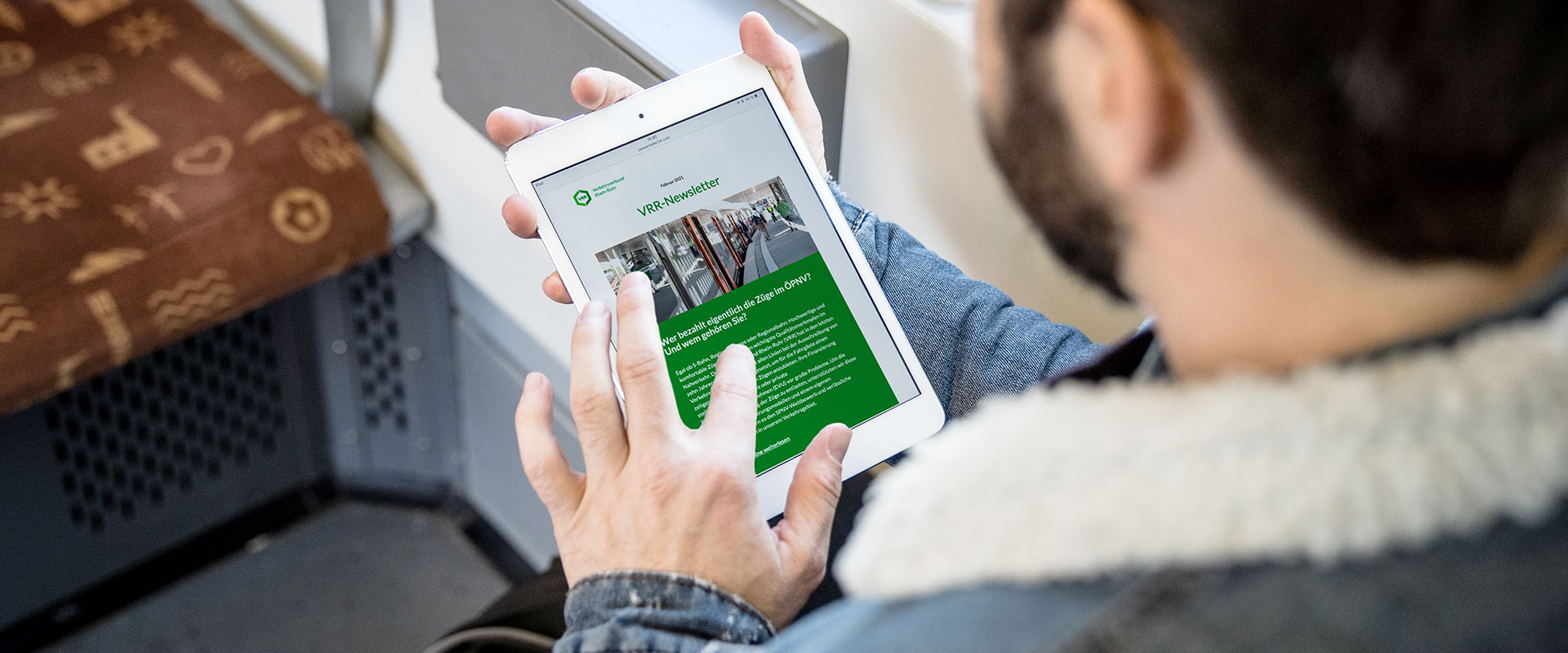 Ein männlicher Fahrgast sitzt im Zug und sieht sich den VRR-Newsletter auf einem Tablet an