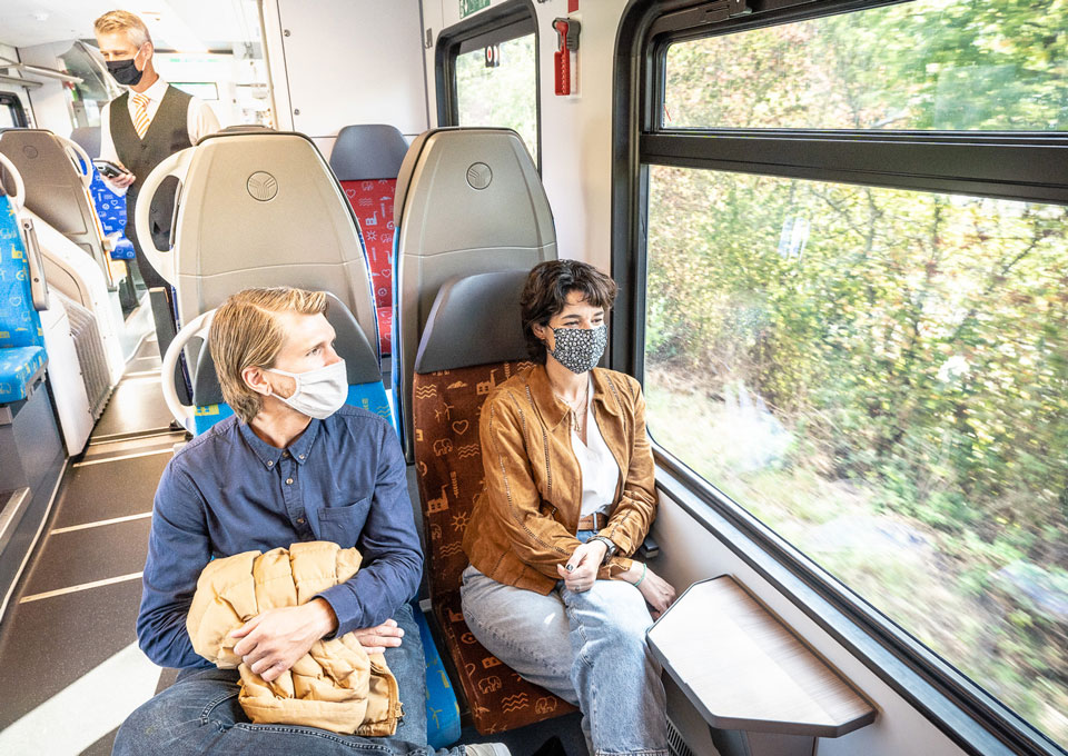 Zwei Menschen sitzen mit der Maske im Zug