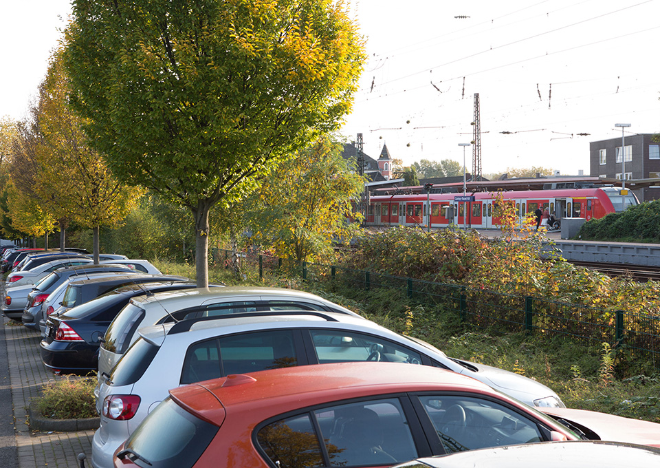Angrenzend an einen Parkplatz fährt eine S-Bahn ab.