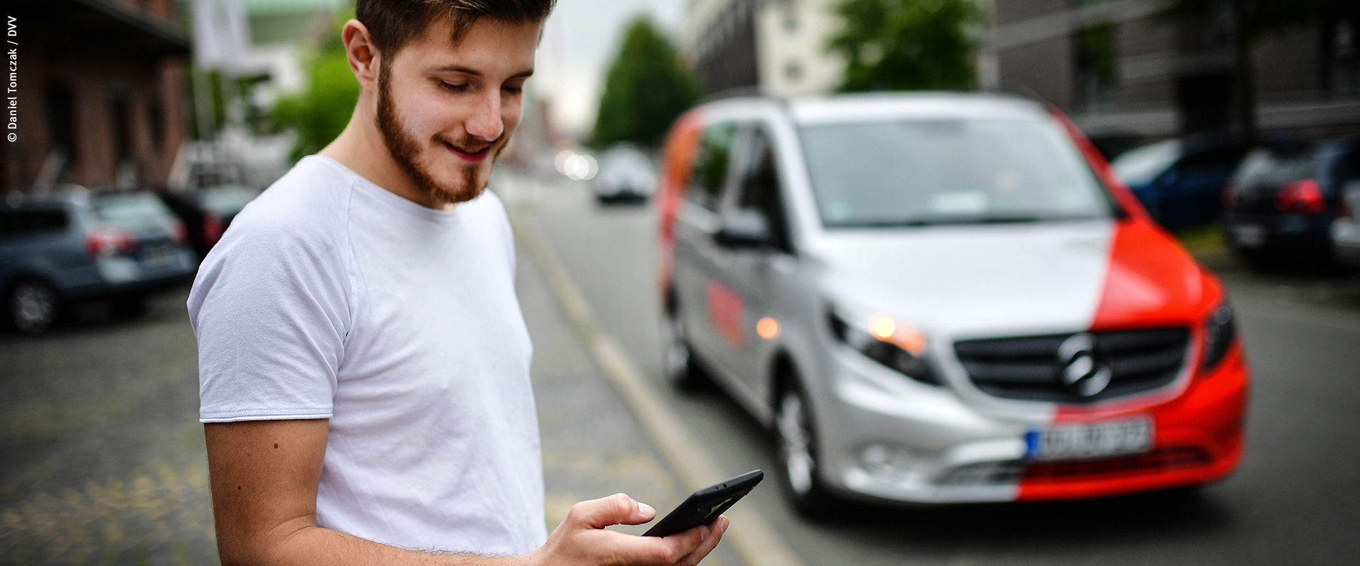 Ein junger Mann steht am Straßenrand und schaut auf sein Smartphone