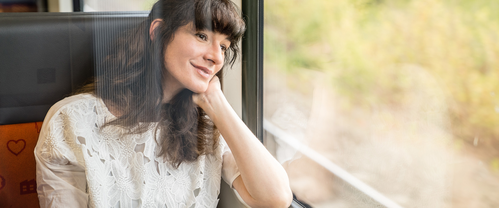 Eine junge Frau sitzt im Zug und schaut aus dem Fenster