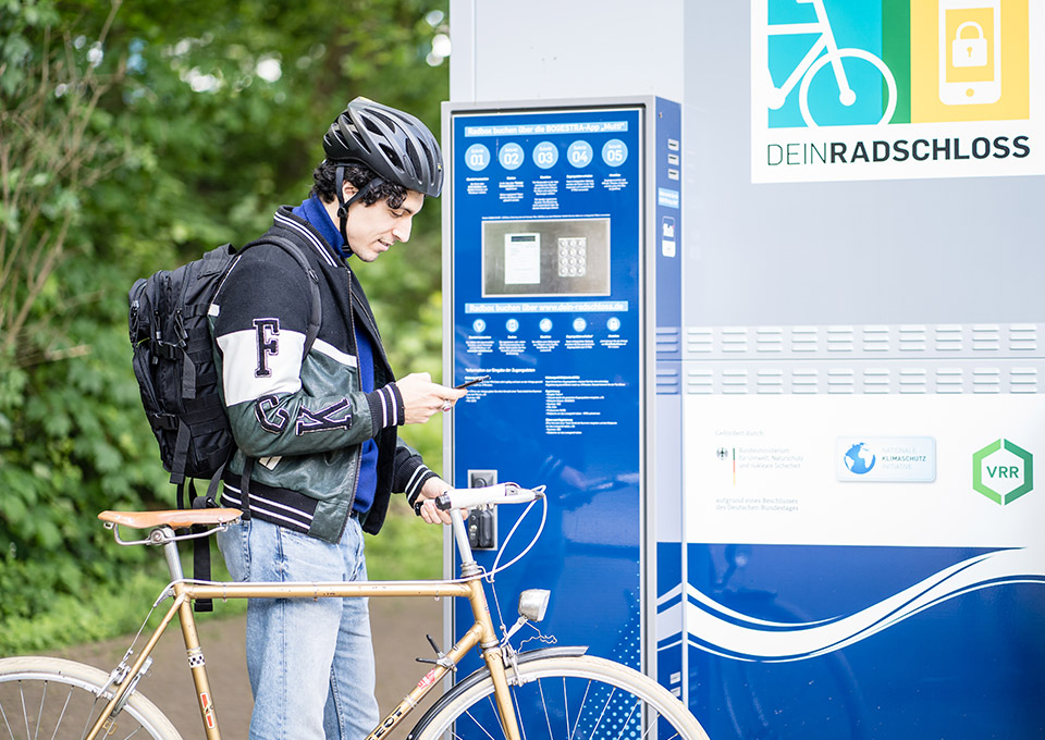 Fahrradfahrer schaut an einer Dein Radschloss Station auf sein Smartphone