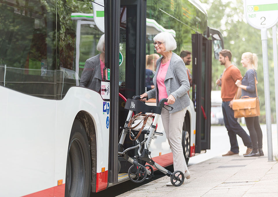 Eine ältere Frau steigt mit ihrem Rollator in den Bus ein