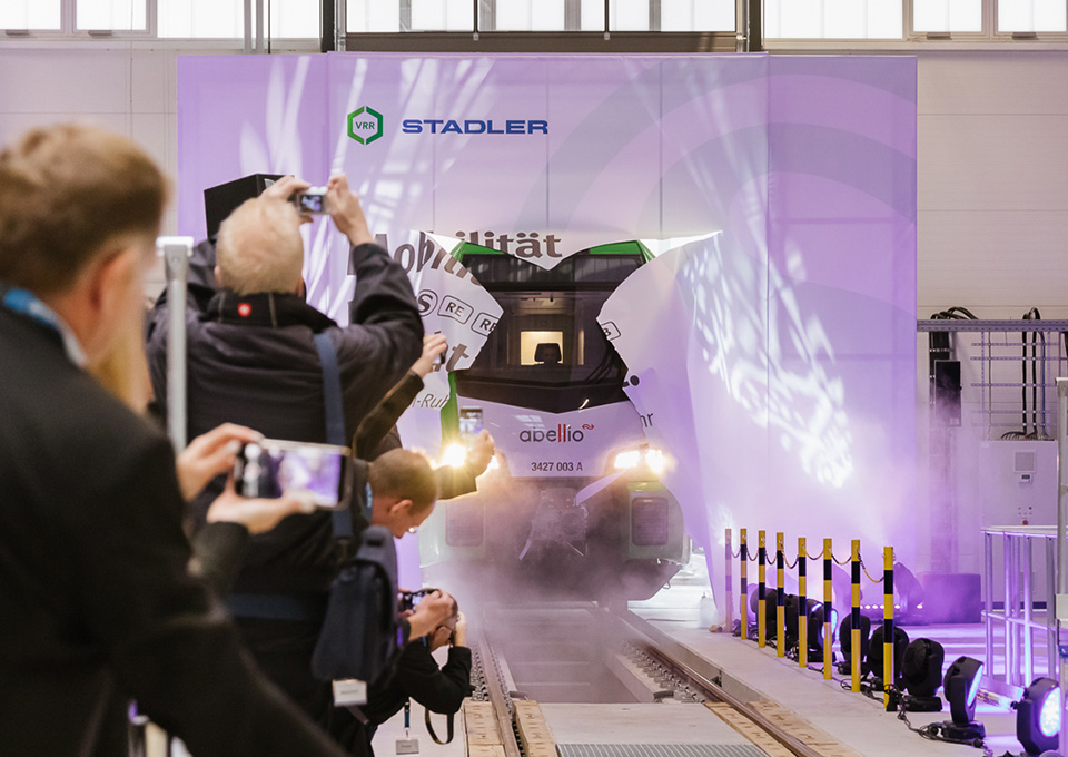 Eine neue S-Bahn im VRR-Design fährt zur Einweihungsfeier durch eine Papierwand in die Werkstatt ein