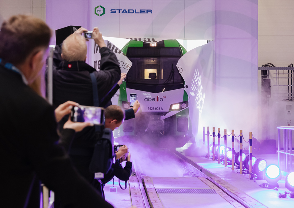 Eine neue S-Bahn im VRR-Design fährt zur Einweihungsfeier durch eine Papierwand in die Werkstatt ein