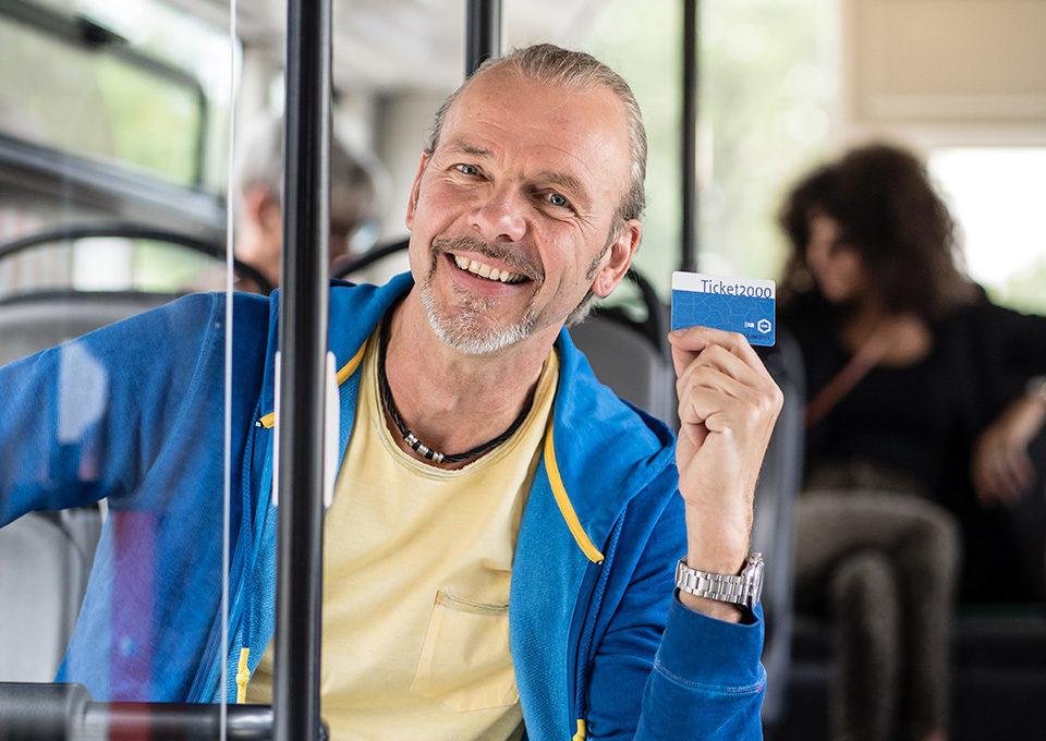 Ein männlicher Fahrgast hält im Bus sein Ticket 2000 hoch