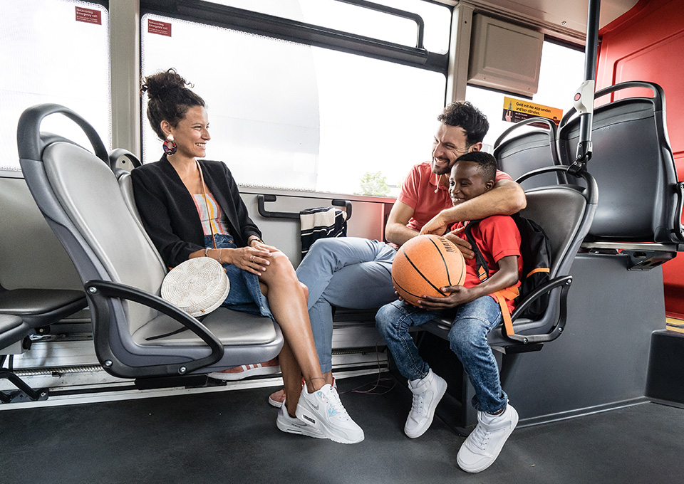 Ein Mann, eine Frau und ein Kind mit Ball sitzen zusammen im Bus