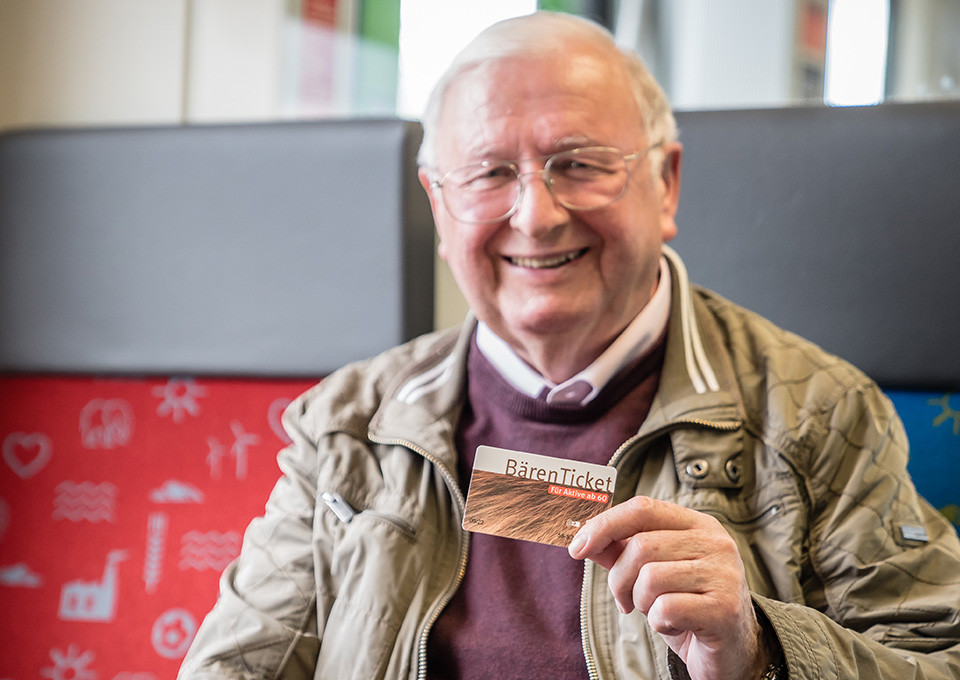 Ein älterer Mann sitzt mit seinem Bärenticket in der Hand im Zug